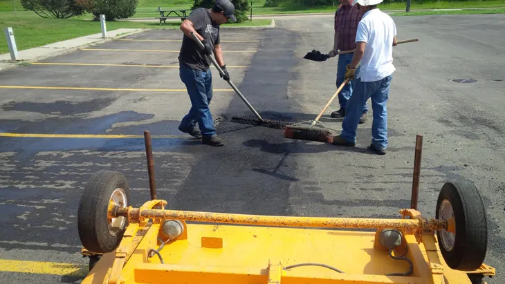 Arrow Asphalt LLC workers repairing asphalt parking lot with sealant and tools.
