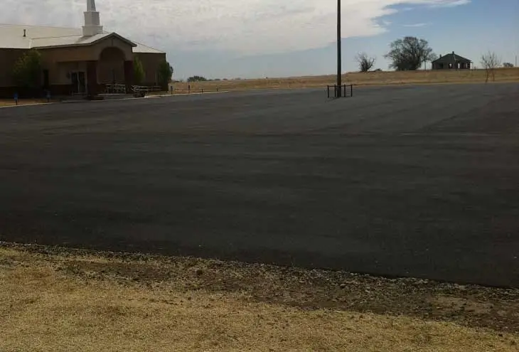 Newly paved commercial parking lot and asphalt overlay with church building in background.