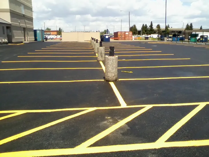 Newly sealcoated asphalt parking lot with yellow parking lines and bollards in Noble, OK.