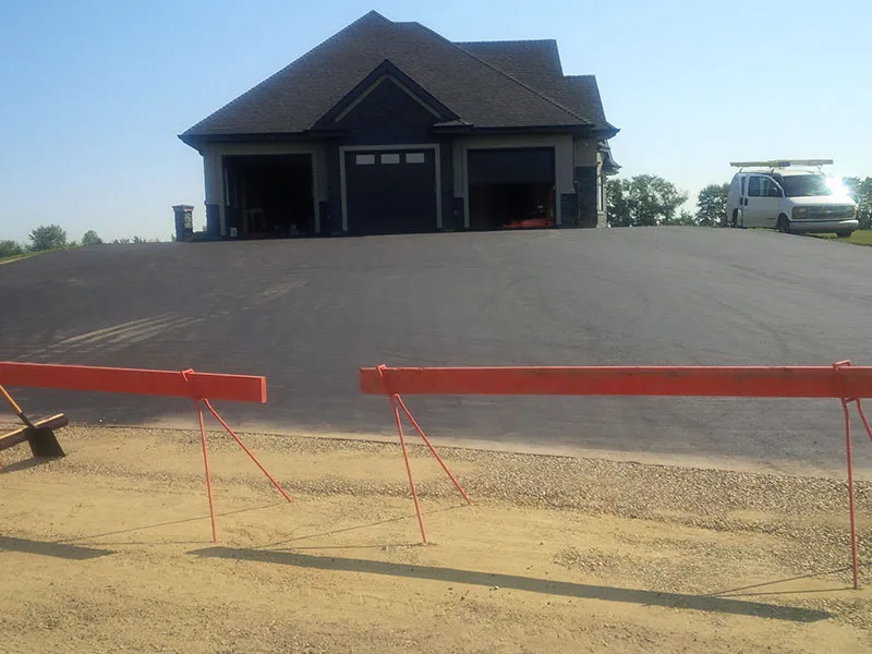 Newly paved asphalt driveway and parking area with construction barricades.