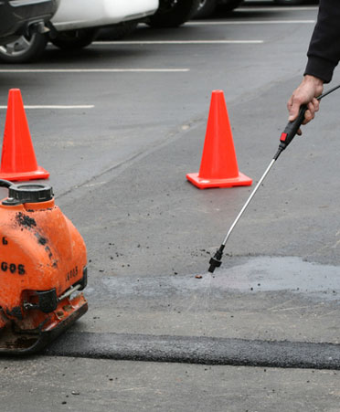 Asphalt repair and maintenance with pressure washer and patching equipment.