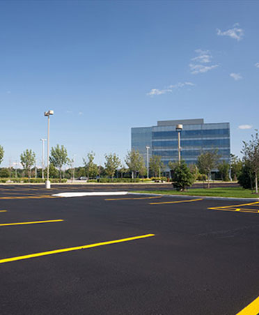 Newly paved commercial parking lot with yellow lines and a modern building in the background.
