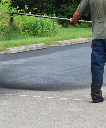Arrow Asphalt LLC worker applying sealcoating to asphalt parking lot surface