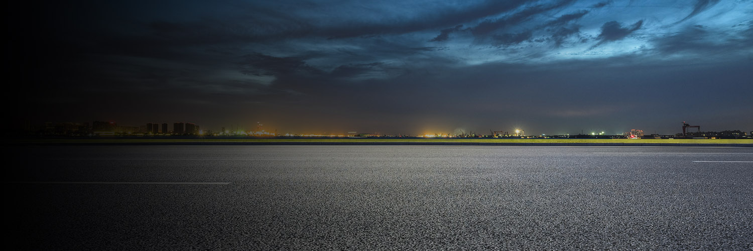 Asphalt parking lot at night with city lights and storm clouds
