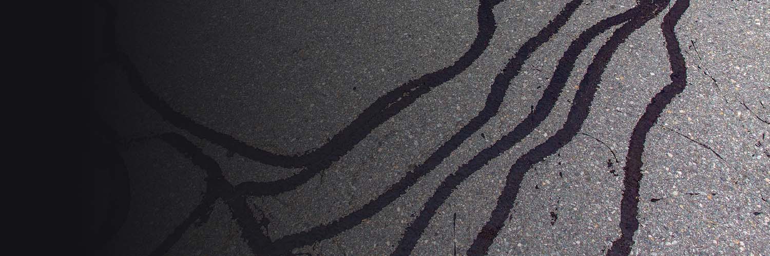 Asphalt cracks being sealed with black rubberized sealant for pavement maintenance.