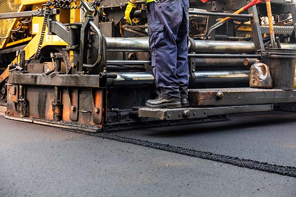 Asphalt paving equipment and worker laying new asphalt surface for overlay application.