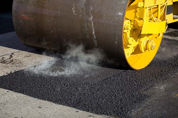 Asphalt roller compacting new pavement for parking lot repair and driveway resurfacing.
