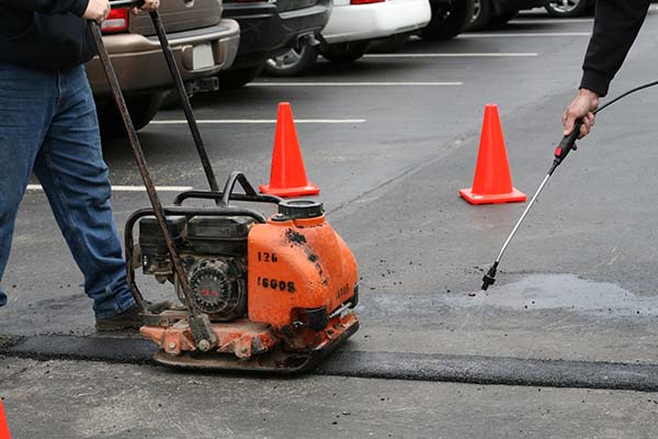 Asphalt crack sealing equipment and worker applying sealant to pavement in Oklahoma City parking lot.