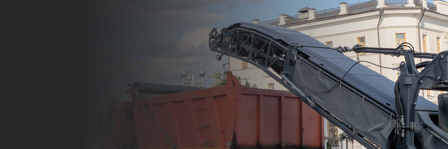 Asphalt milling machine removing pavement material and loading into truck.