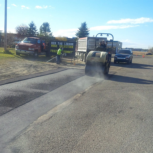 Asphalt paving in Yukon, OK, with roller compacting new pavement near Red Tag Liquor store.
